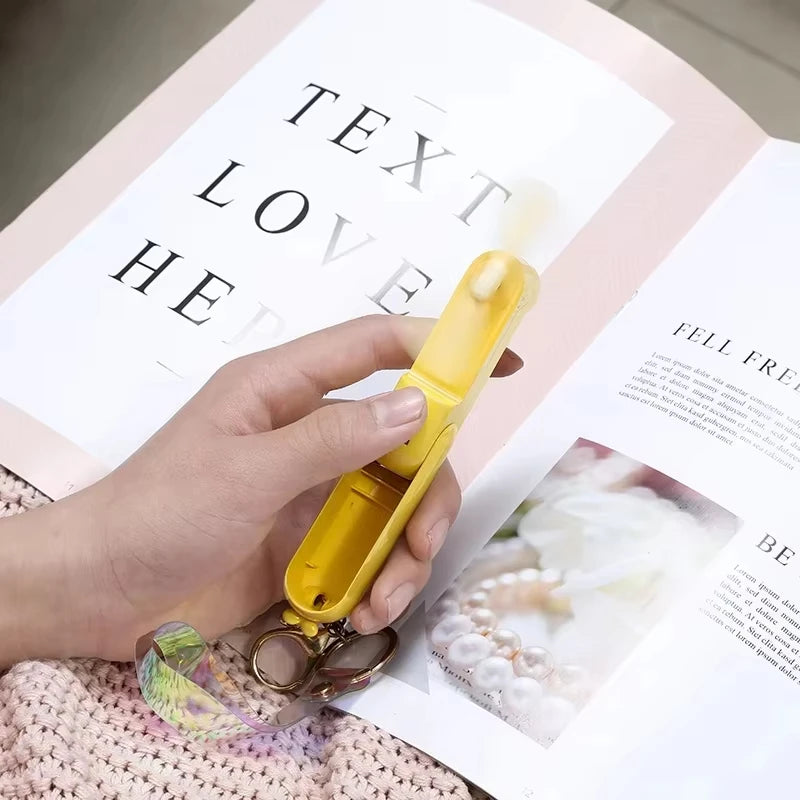 Yellow mini handheld keychain fan held in a hand with a metal key ring.