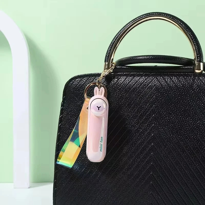Pink mini handheld keychain fan clipped to a black bag with a metal key ring.