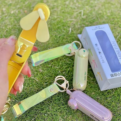 Yellow mini handheld keychain fan with a ribbon strap and metal key ring outdoors.