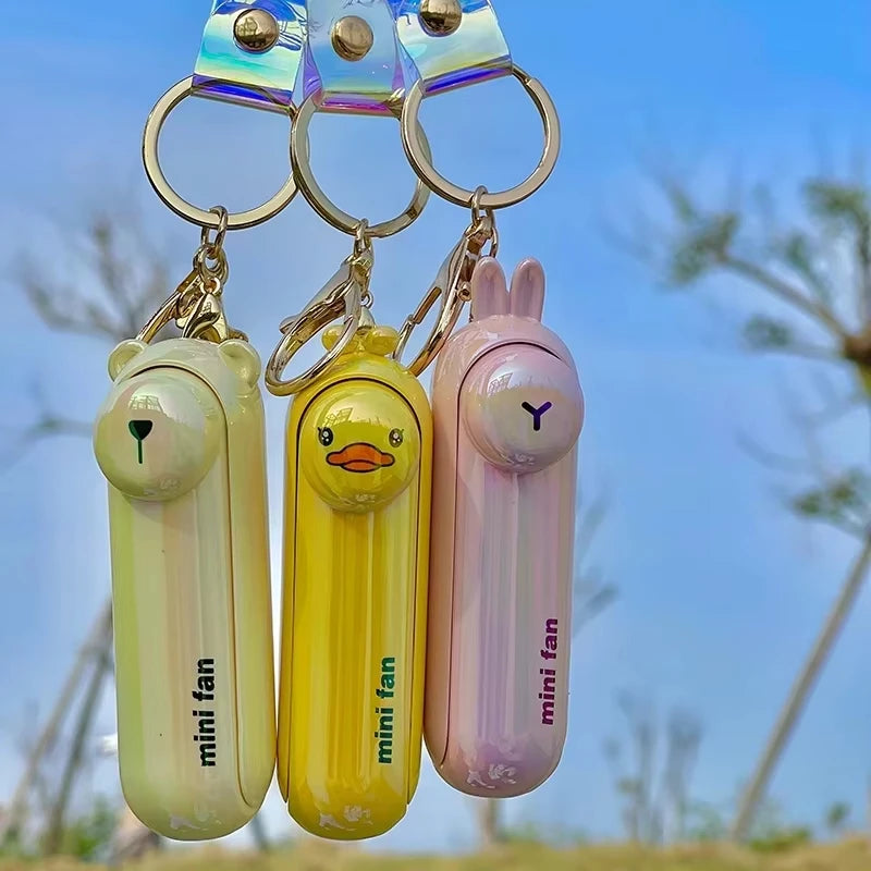 Three mini handheld keychain fans hanging: green, yellow, and pink with metal rings.